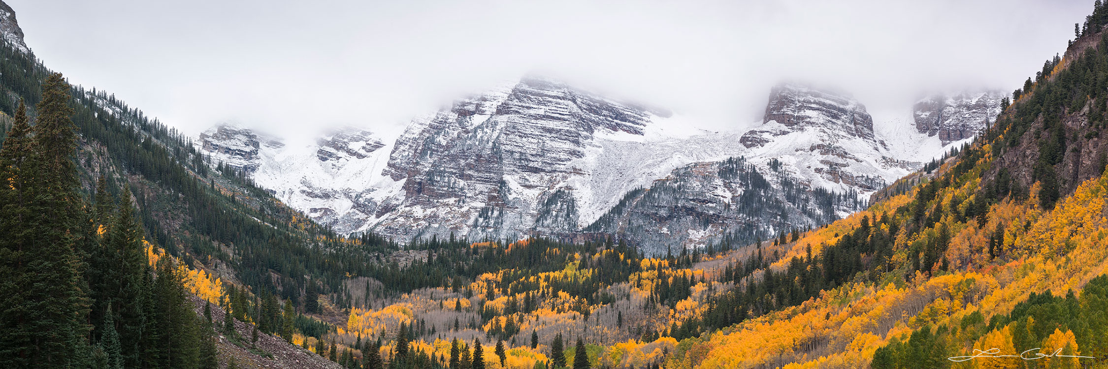Yellow aspen panorama and Maroon Bells covered in clouds