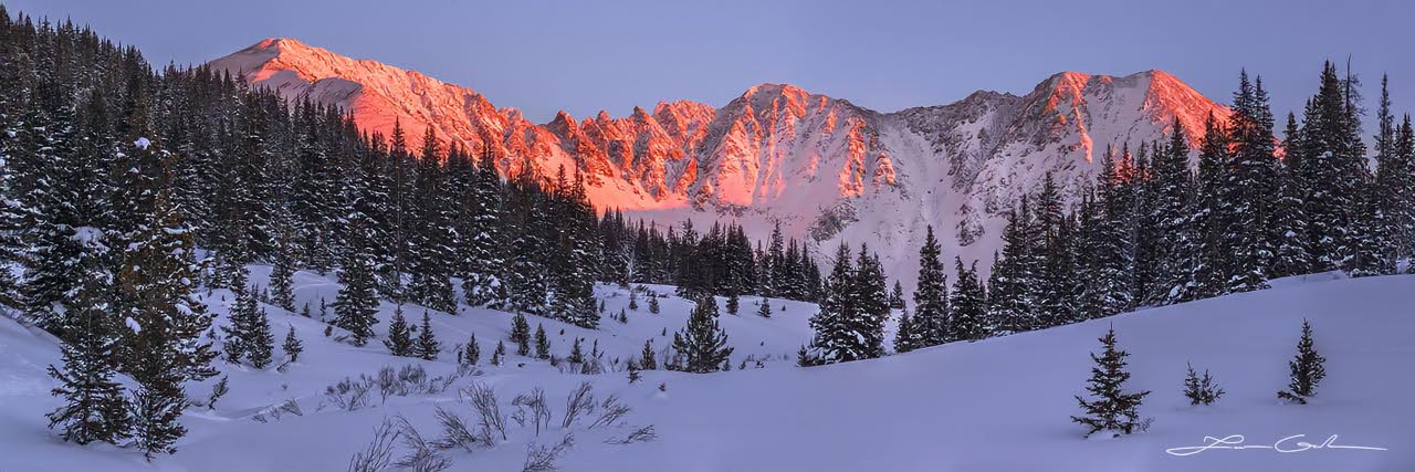 Snow covered meadow and pine trees with red jagged mountains in a sunset - Small
