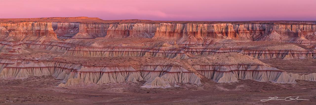A colorful canyon with red stripes and brown sandstone with pink sunrise clouds above - Small
