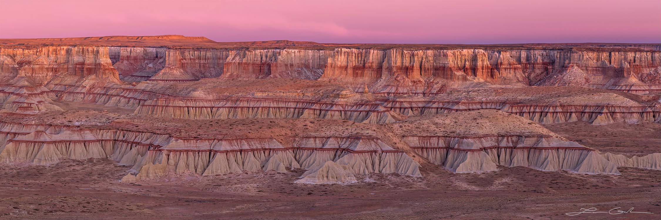 A colorful canyon with red stripes and brown sandstone with pink sunrise clouds above