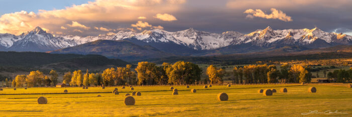 A large ranch meadow with hay bales and beautiful snow covered Colorado mountains