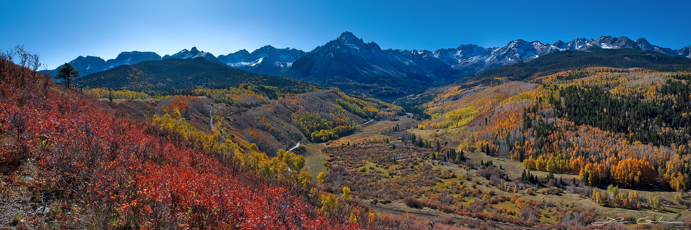 Red and orange fall colors of trees, shrubs around a beautiful valley and big mountains with blue skies