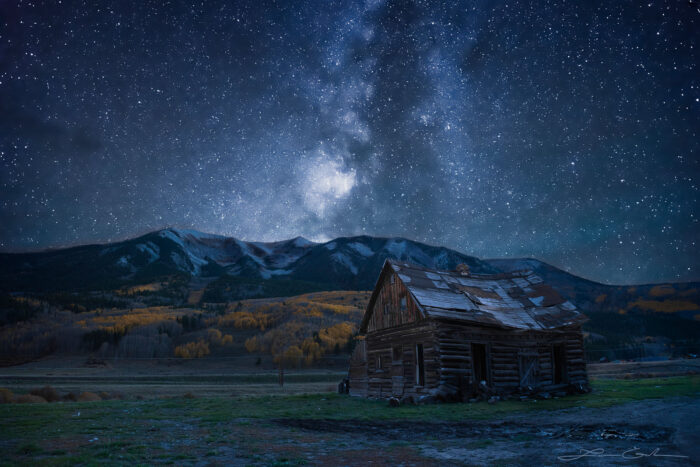 Nigh shot of an old barn, yellow aspen trees and mountains under a starry sky with the milky way