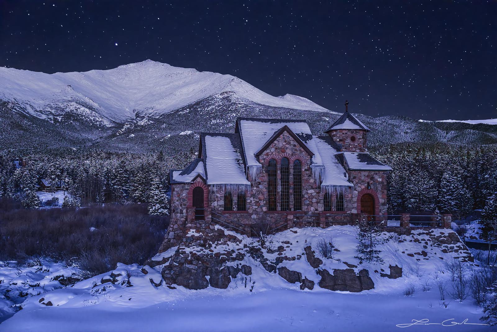 Charming stone church at the base of a mountain on a winter night under stars