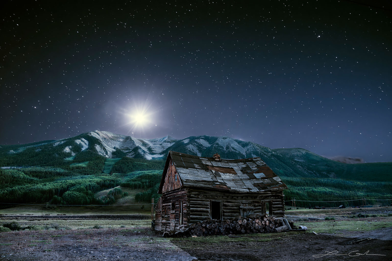 An old barn with mountains around and stars and moonlight