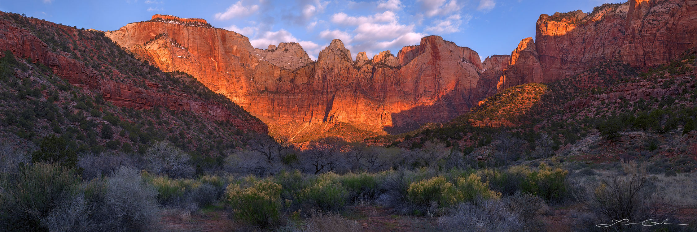 Beautiful red mountains with a stripe of sun light across and a desert valley with trees and shrubs, Zion National Park