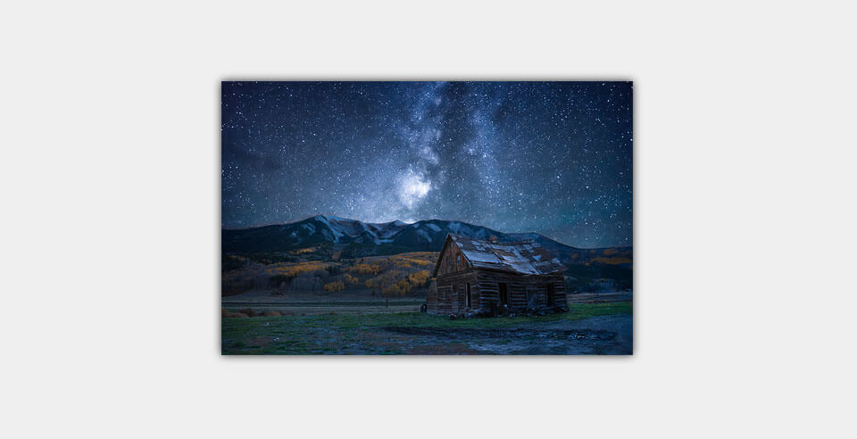 A print of the milky way, mountains, and a barn on a light grey wall