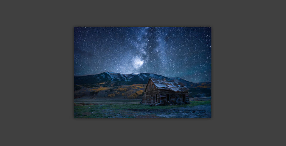 A print of the milky way, mountains, and a barn on a dark grey wall