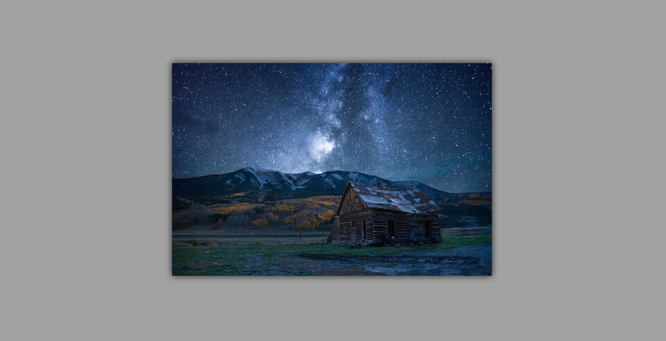 A print of the milky way, mountains, and a barn on a grey wall