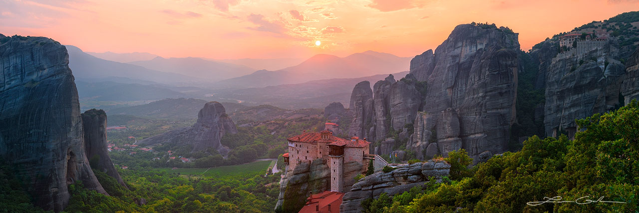 A monastery on top of a cliff with the setting sun in the distance, Meteora, Greece - Small
