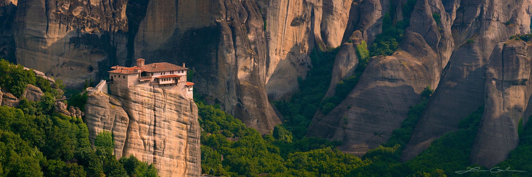 A panorama of a small monastery on the edge of a tall vertical cliff, among other tall cliffs, Meteora