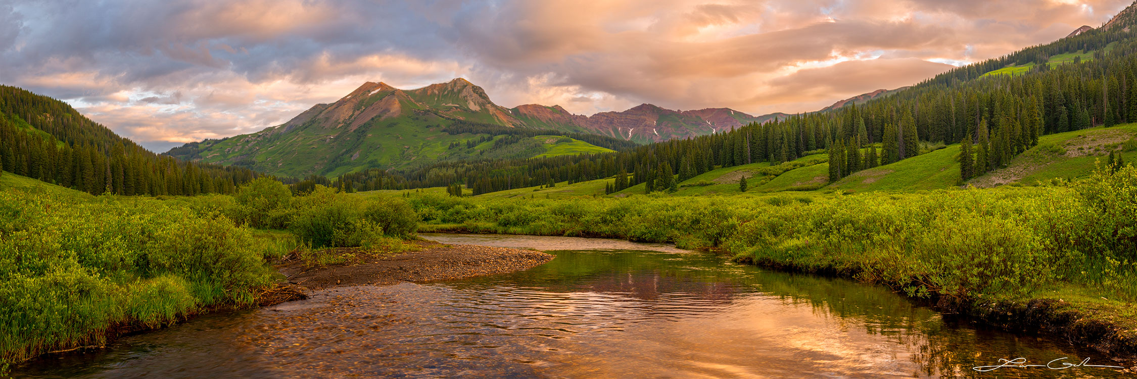 A mountain river in a beautiful green valley with pine trees and pretty mountains during sunrise