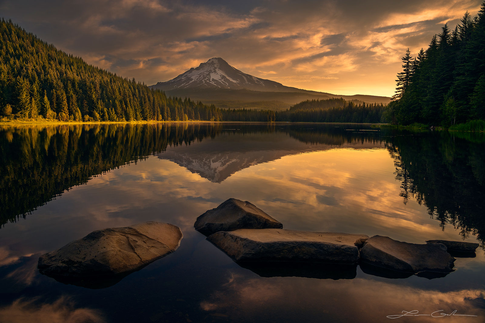 Mt Hood at sunrise and its reflection in a calm mountain lake surrounded by evergreen trees, Oregon