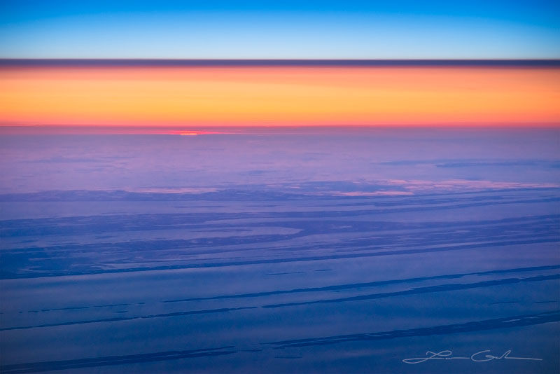 An aerial sunset with blue sky, red light band and land below - Small