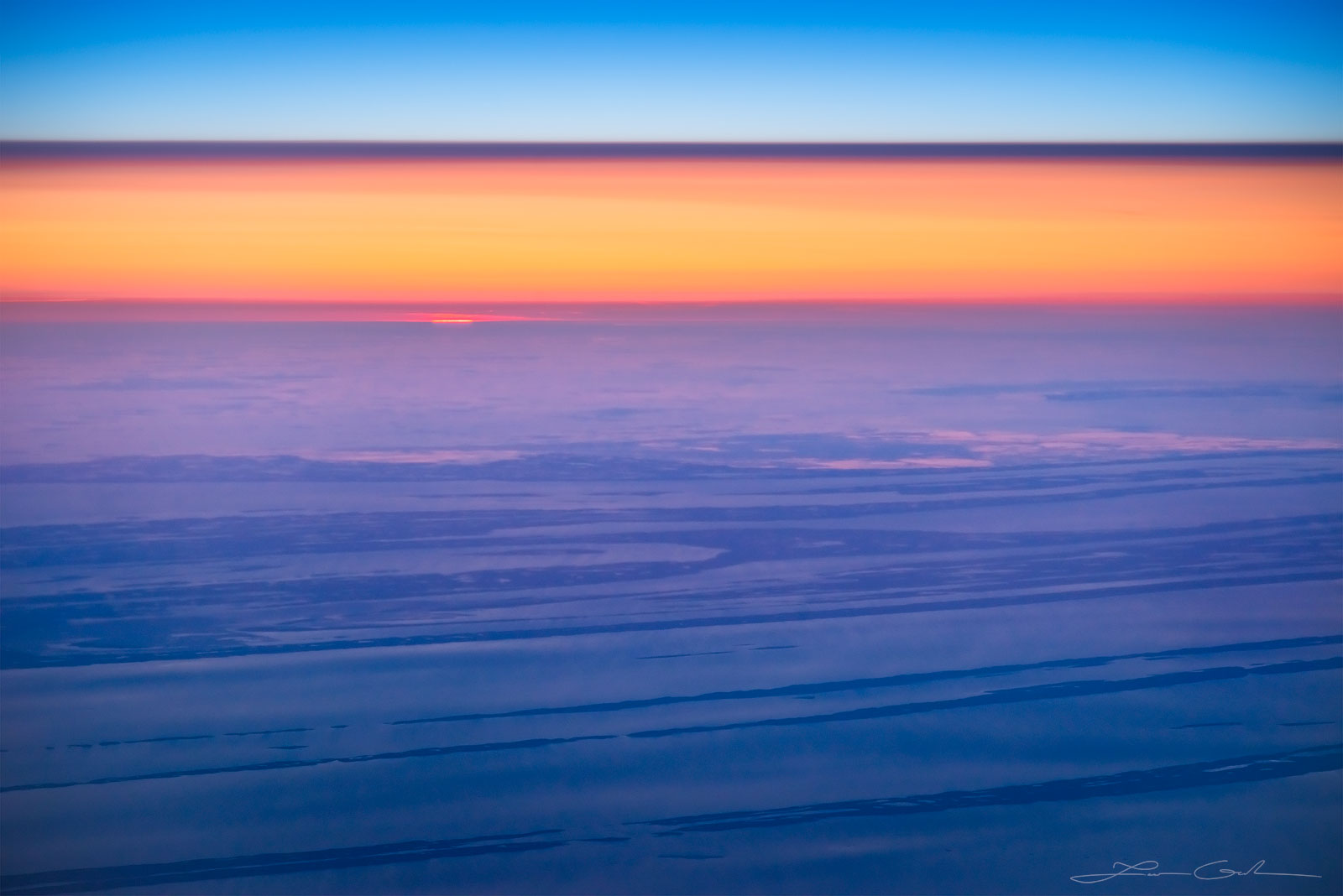 An aerial sunset with blue sky, red light band and land below