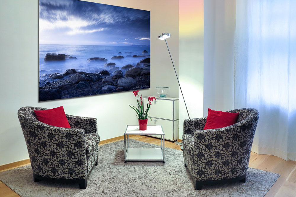A photo print of an ocean shore on a wall in a room with two armchairs and a table with flowers