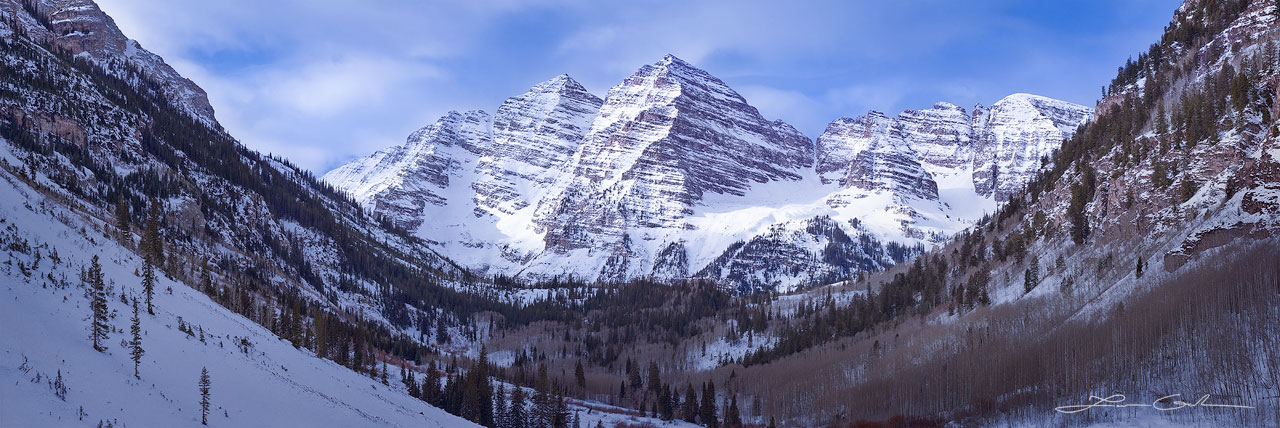 A winter panorama of Maroon Bells, Colorado with snow covered mountains and aspen and evergreen trees - Small