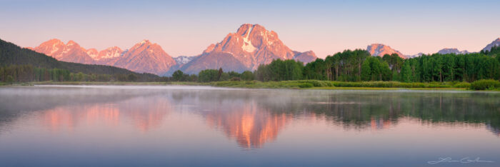 Calm water of the Snake river at Oxbow Bend in Grand Tetons National Park, with a reflection of Mount Moran at sunrise.