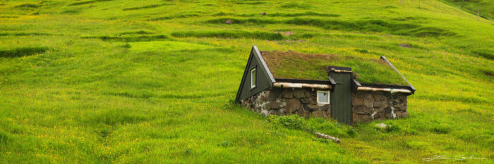 A tiny house structure in the middle of a wildflower hill which looks like the house of Frodo - Faroe Islands - Gintchin Fine Art