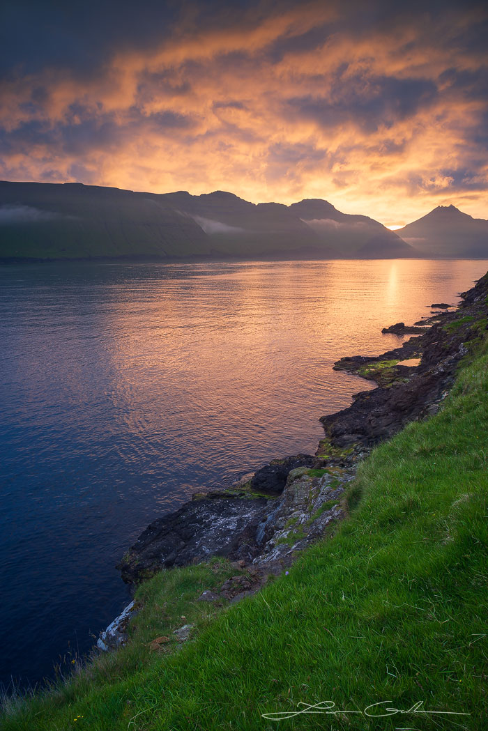 Faroese sunset with orange clouds and light reflecting in the ocean fjord - Faroe Islands - Gintchin Fine Art