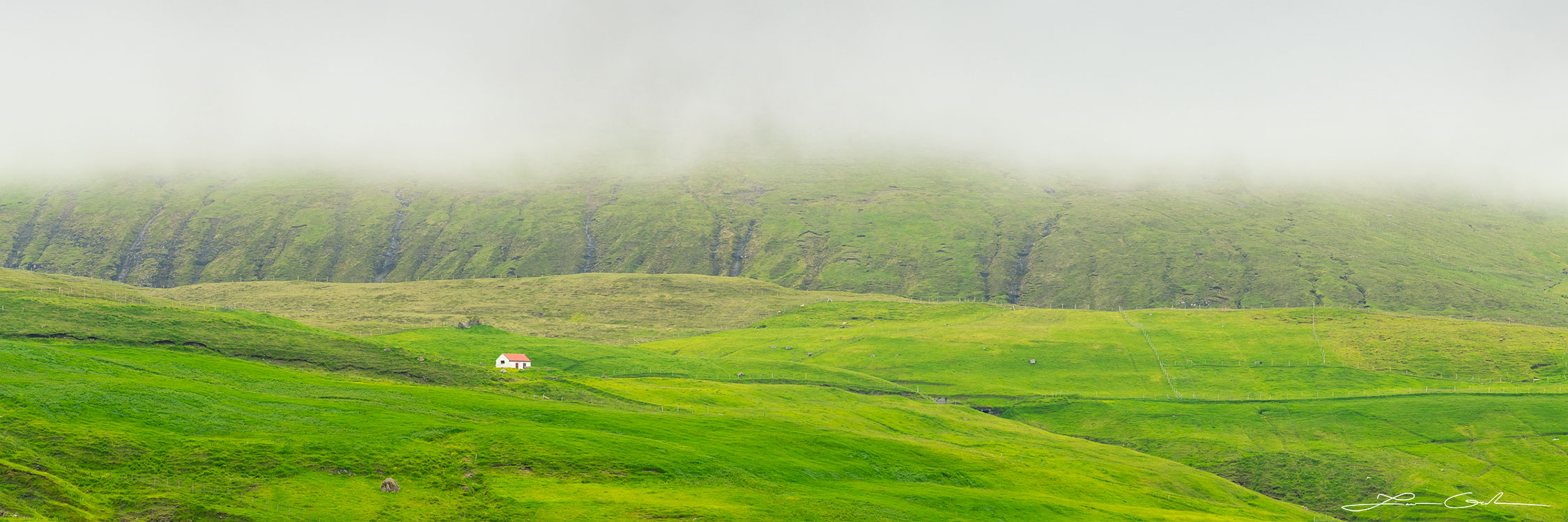 A solitary house on top of a lush green hill and heavy fog above - Faroe Islands - Gintchin Fine Art