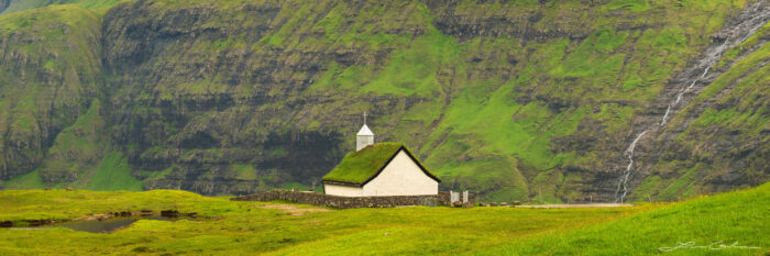 A panoramic photograph of a church surrounded by mountains and a waterfall - Faroe Islands - Gintchin Fine Art