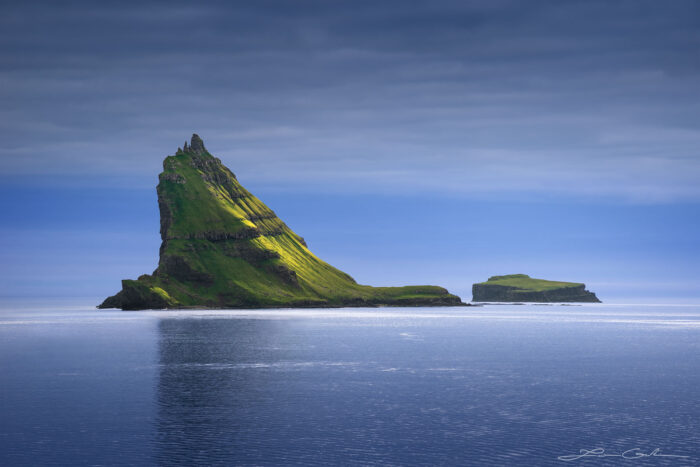 A tall steep mountain island covered with green grass and sunshine glow - Faroe Islands - Gintchin Fine Art