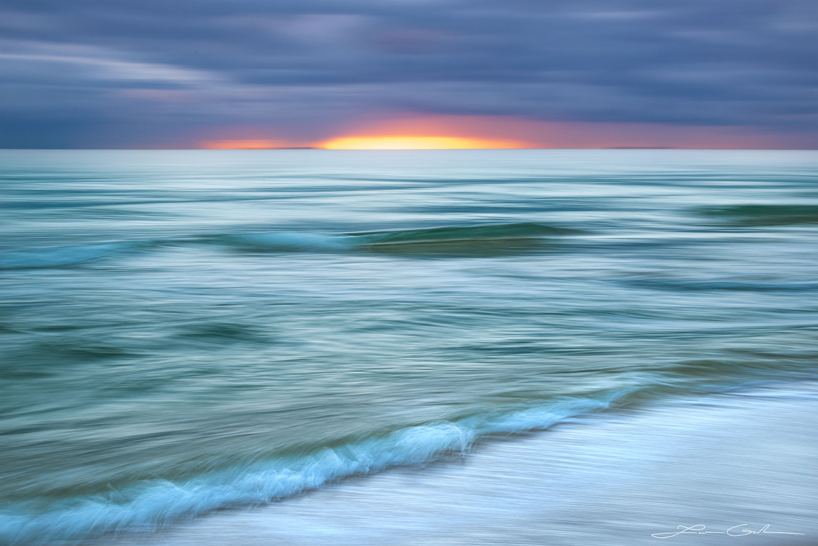 A glassy looking ocean shore with some waves and a sunrise on the horizon - abstract photo - Gintchin Fine Art