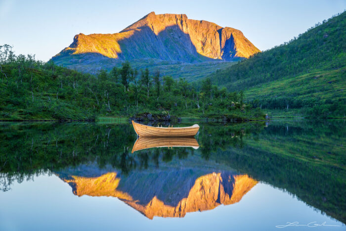 A beautiful mountain at sunrise and boat in a calm lake with a reflection in Norway - Gintchin Fine Art