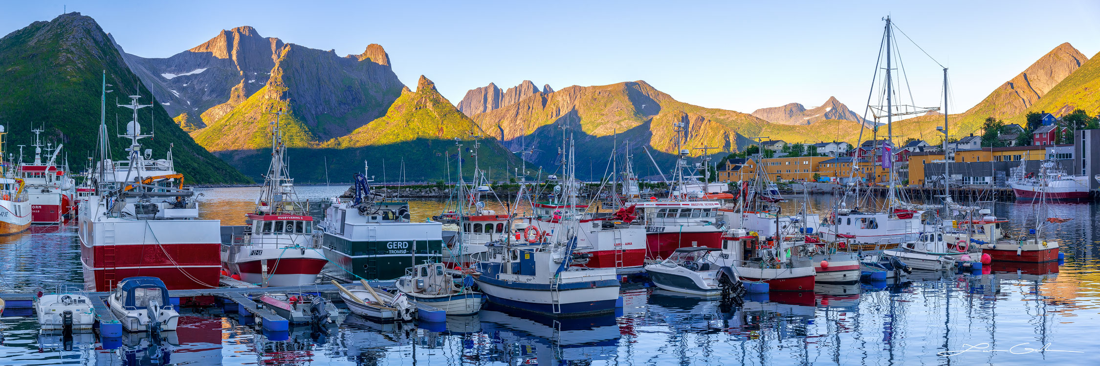 A panoramic picture of a fishing boat harbor with beautiful mountains in Senja, Norway - Gintchin Fine Art