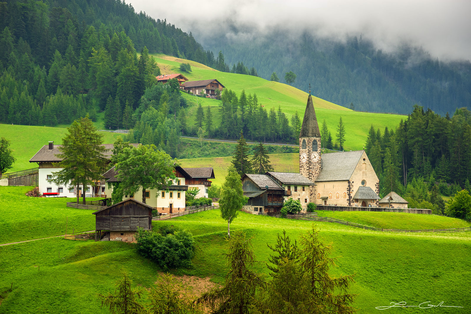 A mountain village and a church in the Italian Dolomites with green meadows and forests - Gintchin Fine Art
