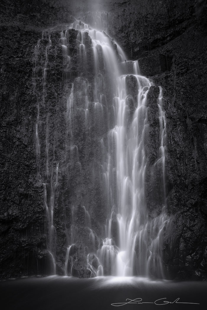 Black and white fine art photo print featuring a detailed slow-motion waterfall cascading over stark black rocks into a tranquil pool - Gintchin Fine Art.