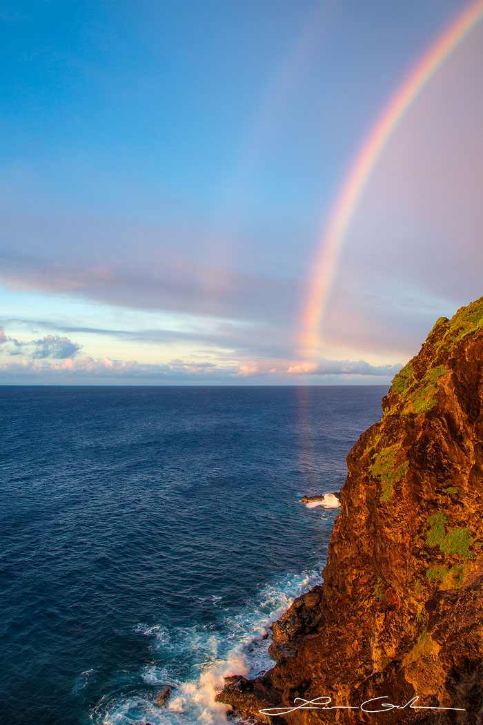 Fine art photo print of Maui's vertical cliff, calm ocean, and a magical double rainbow stretching from the blue sky to the sea - Gintchin Fine Art.