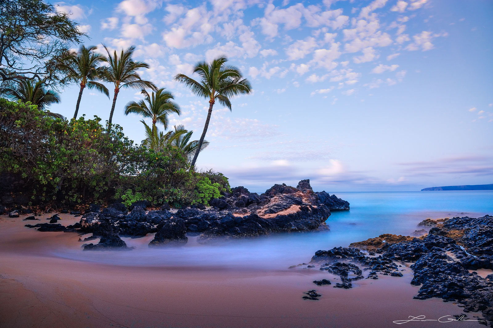 Slow motion, long exposure image of a secluded rocky beach in Hawaii, featuring an ethereal mist-like ocean, sand, lava rocks, palm trees, and a tranquil morning sky - Gintchin Fine Art.