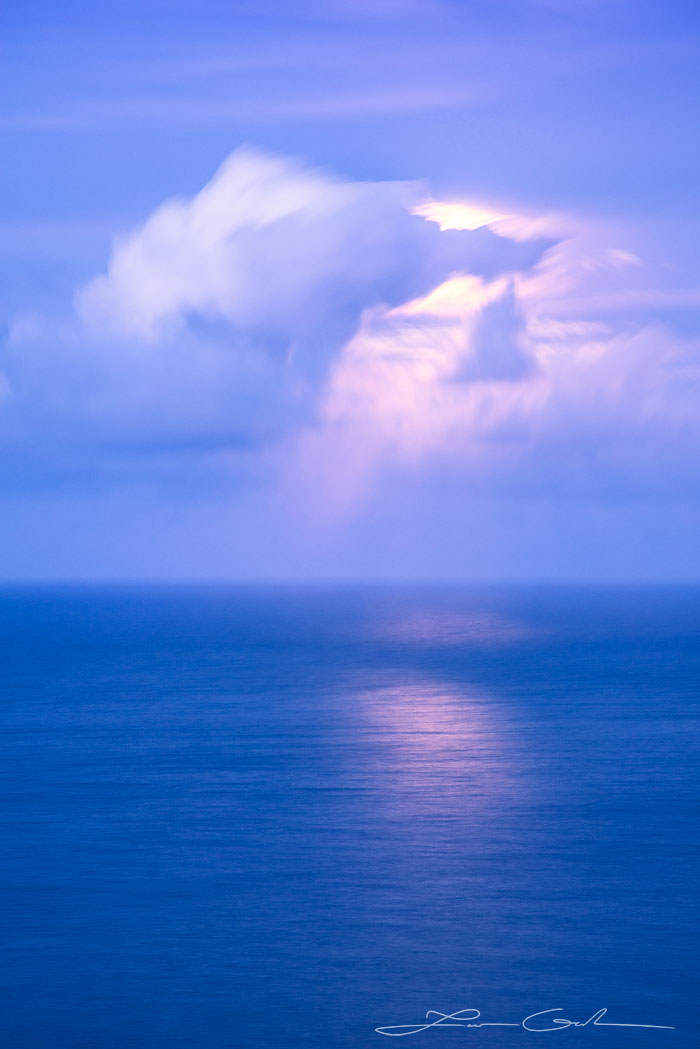 Shy Moon - A captivating fine art print capturing an abstract ocean moon in Hawaii. Predominantly blue tones create an atmosphere of tranquility and mystery. Witness the moon's hidden glow permeating through wispy clouds, reflecting upon the calm and deep blue ocean. Experience the enchantment of nature with this evocative artwork by Gintchin Fine Art.