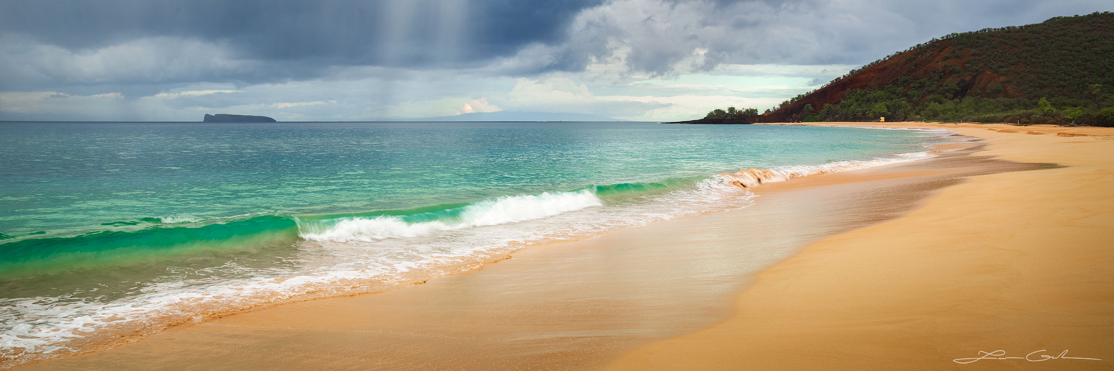 Panoramic view of an empty Maui beach with smooth golden sands, a calm turquoise ocean, a distant view of Molokini island, a hillside meeting the ocean, and a sky filled with dark clouds and falling rain in the fine art print 'Solitude Sands' - Gintchin Fine Art