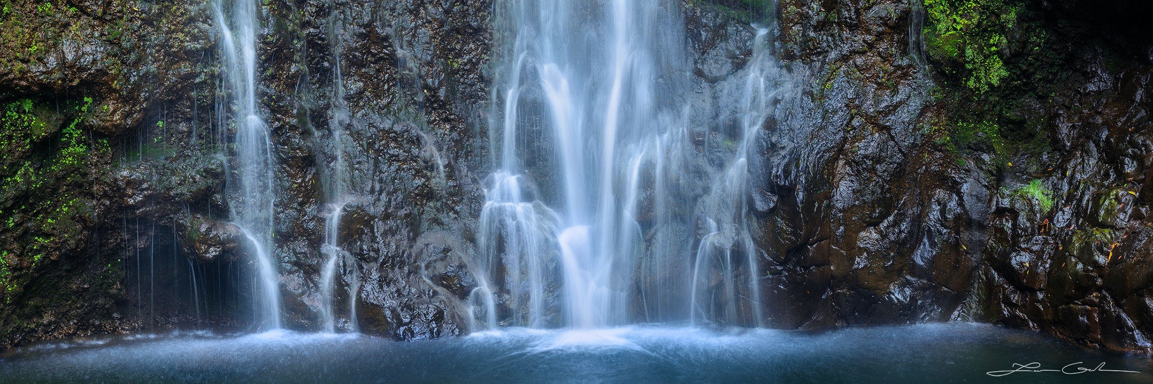 Panoramic waterfall in Hawaii, 'Water Silk' fine art print showing silky water cascading down a dark rock face with moss and small plants, ending in a splash at the pool below - Gintchin Fine Art.