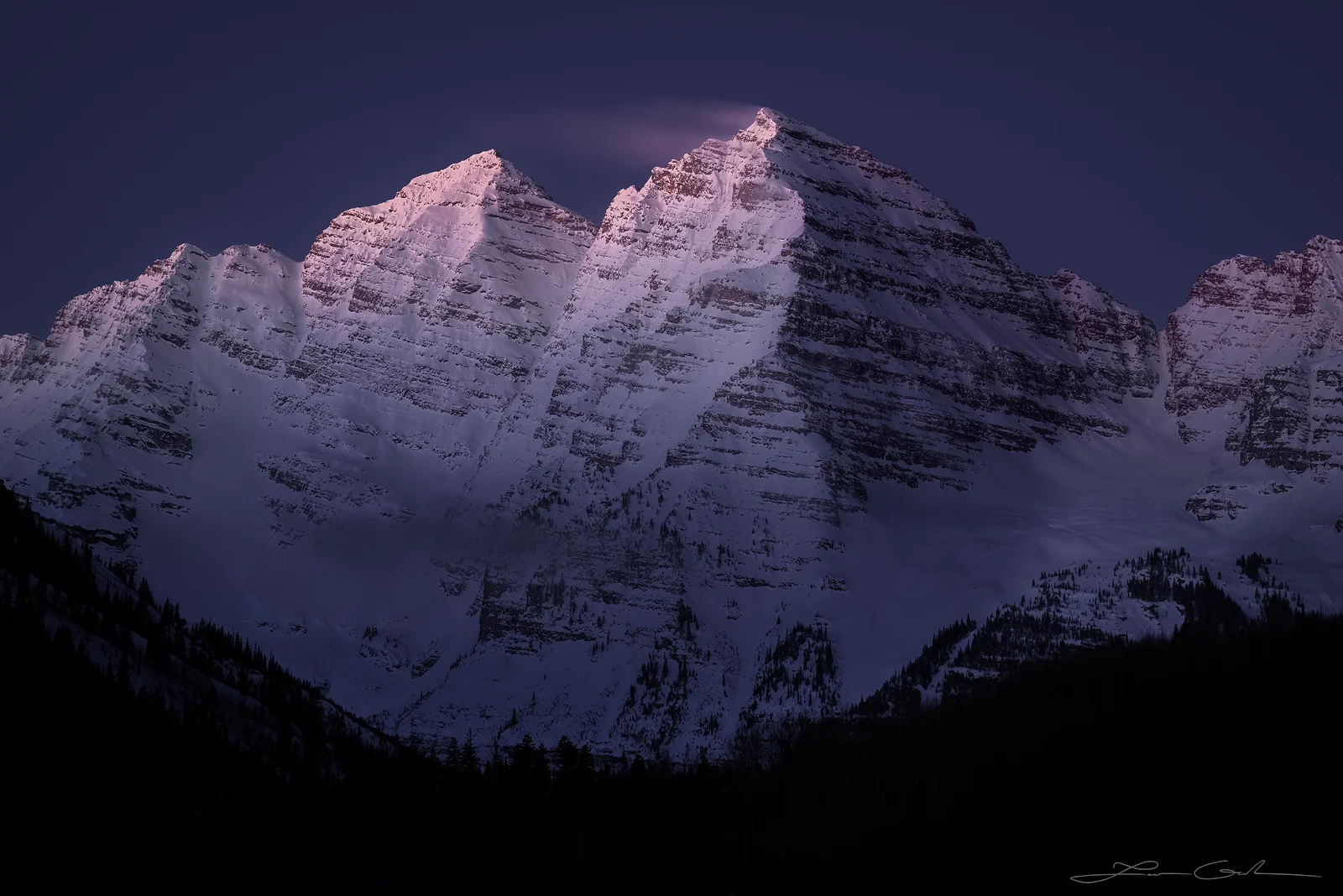 Maroon Bells at dawn in winter, with soft light revealing the peaks and a surreal flow of snow in the air. - Gintchin Fine Art