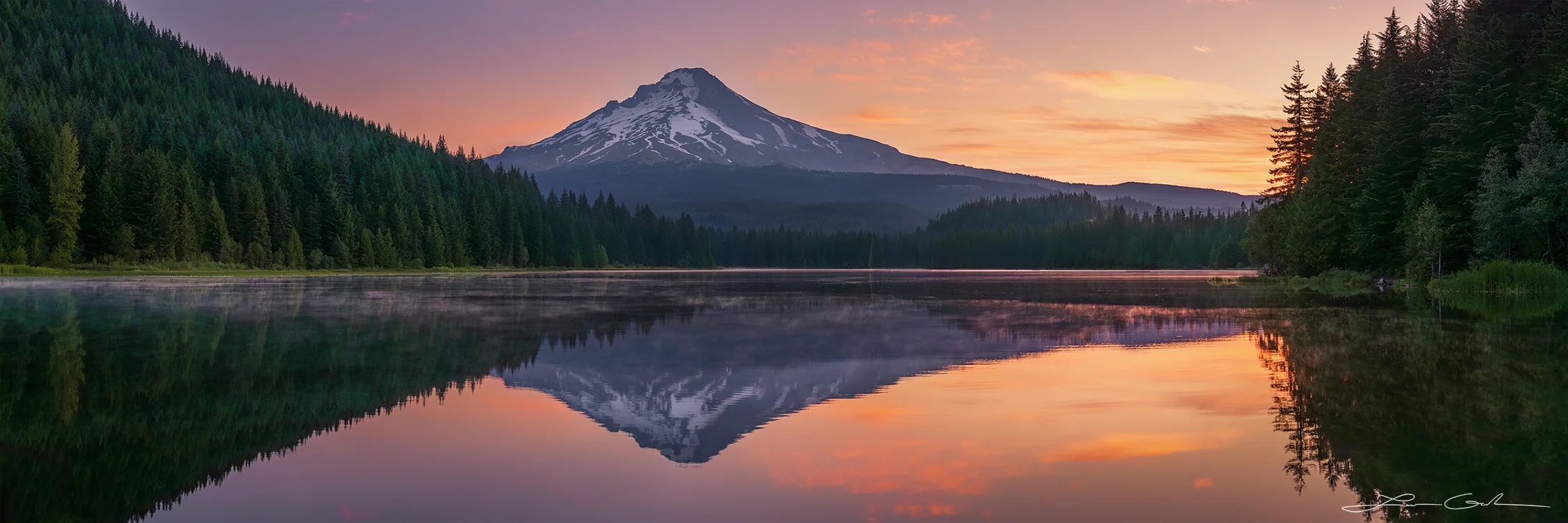 A majestic Oregon mountain sunrise reflected in a still lake. A colorful sunset paints the sky and reflects on the calm water of a lake, with a silhouette of a mountain in the distance. It is Mount Hood, a snow-capped peak, is reflected in the still waters of Trillium Lake at dusk. - Gintchin Fine Art