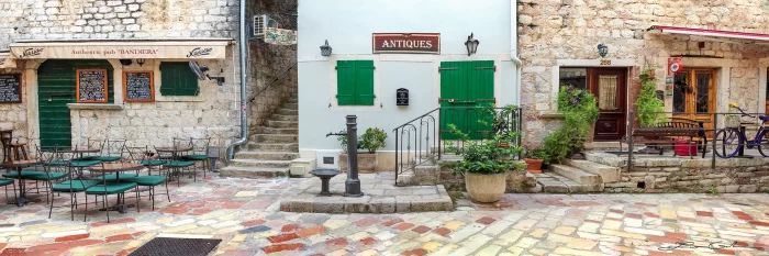 Fine art photo print of a cobblestone European street in Old Town Kotor, Montenegro, featuring cafes, antique shops, green shutters, and a vintage bicycle. - Gintchin Fine Art