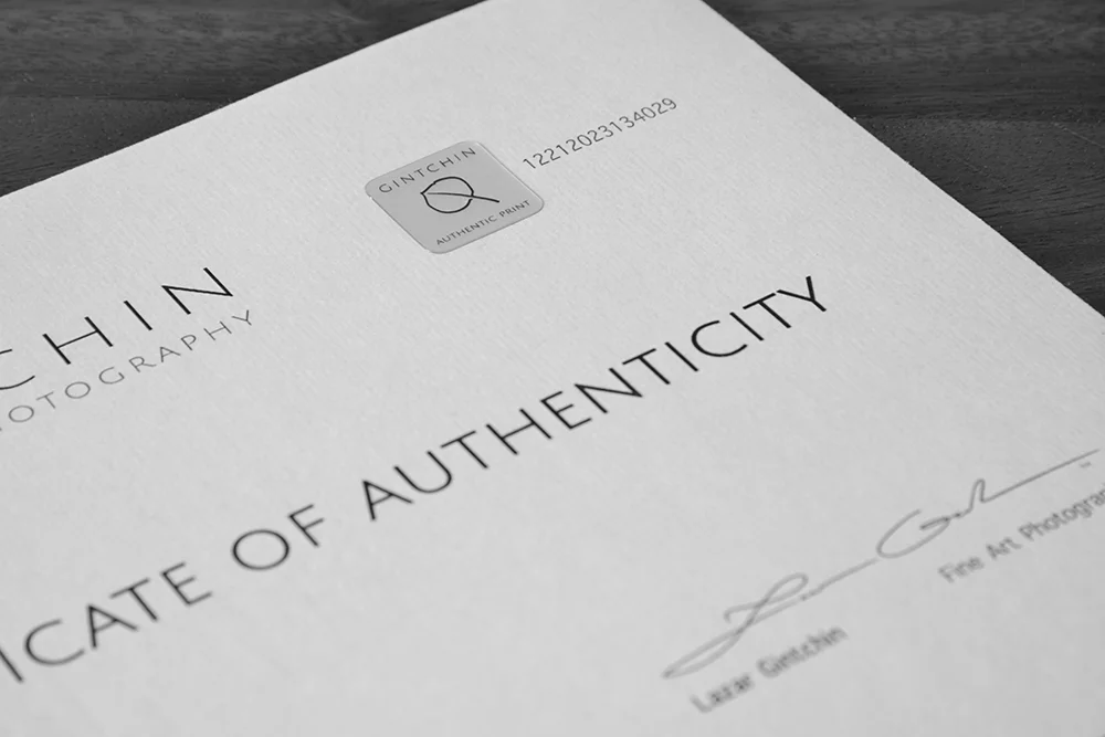 A focused view on the top section of a "Certificate of Authenticity" from Gintchin Fine Art Photography, showcasing the authenticity hologram with the Gintchin logo, unique serial number, and the artist's signature.