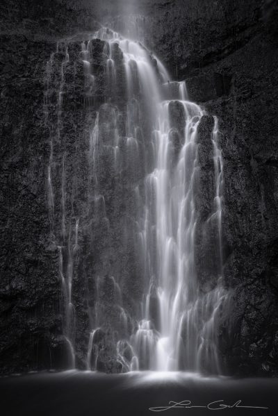 Black and white fine art photo print featuring a detailed slow-motion waterfall cascading over stark black rocks into a tranquil pool - Gintchin Fine Art.