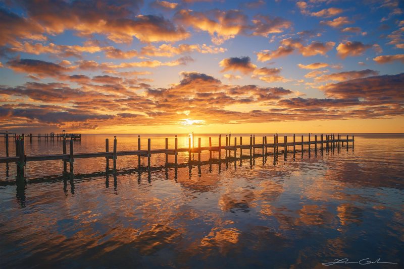 An intense and beautiful Florida sunrise with a wooden pier and calm ocean water - Gintchin Fine Art